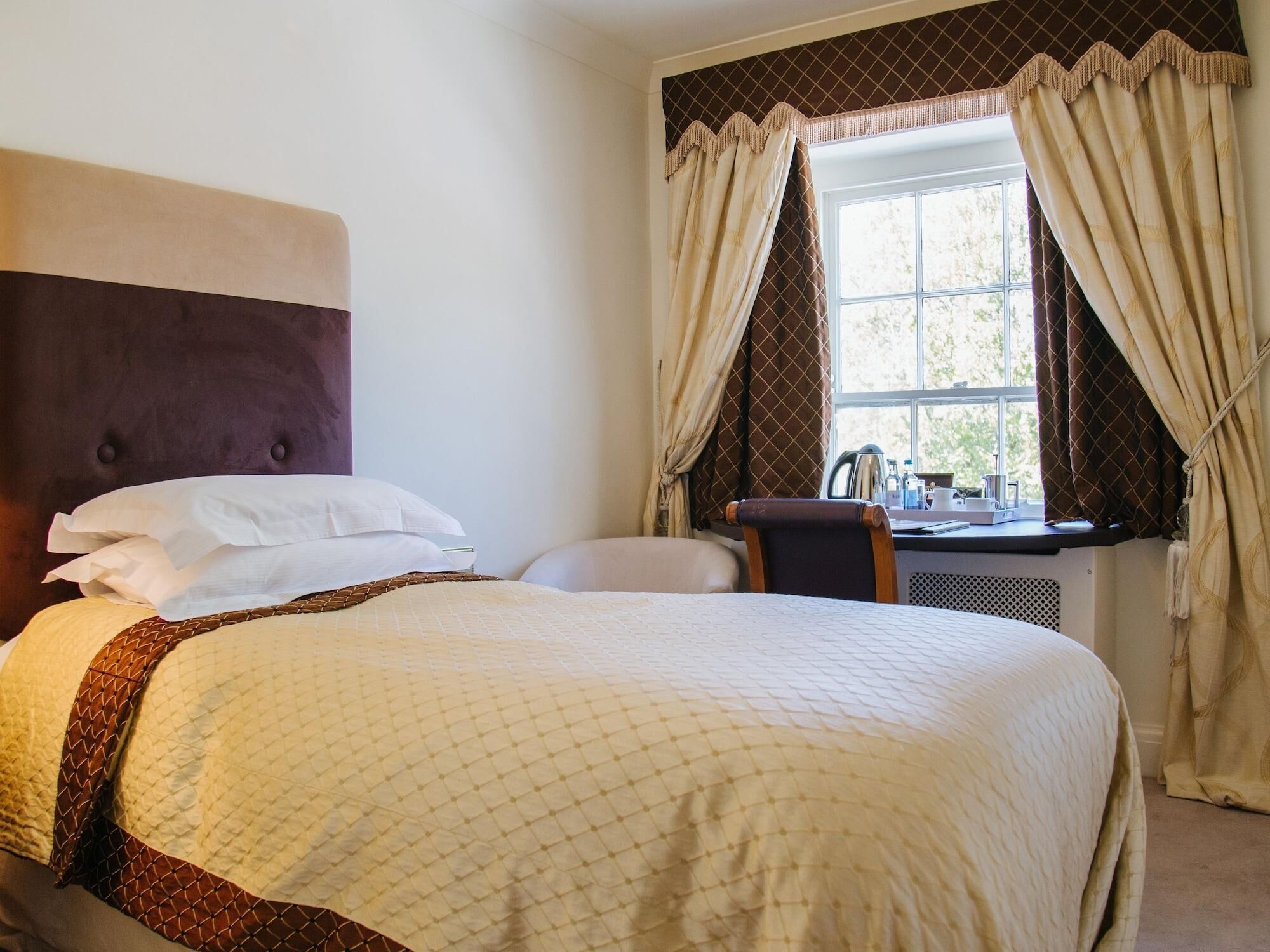 A hotel room with a large bed, a desk with a chair, and a window with curtains.