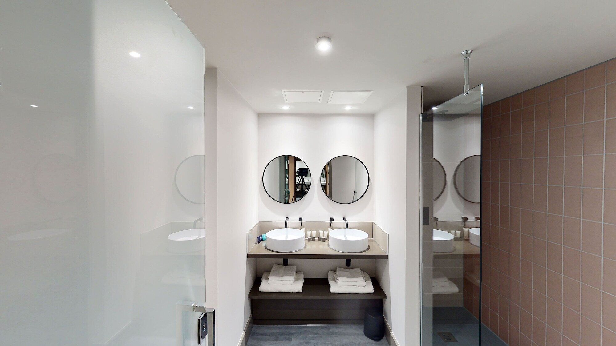 Un bagno moderno con due lavabi, due specchi rotondi e un box doccia in vetro.
