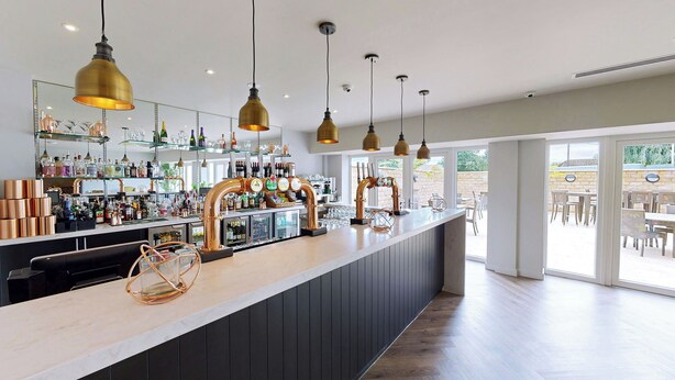 A bar area with copper faucets, hanging pendant lights, and a variety of bottles and glasses on shelves. - Hotel Van Dyk (Chesterfield)