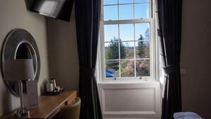 Une chambre d’hôtel équipée d’un bureau, d’une télévision, d’une fenêtre avec des rideaux et d’un lit avec une couverture.