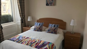 Une chambre d’hôtel avec un grand lit, deux tables de chevet, une fenêtre avec des rideaux et un tableau au mur.