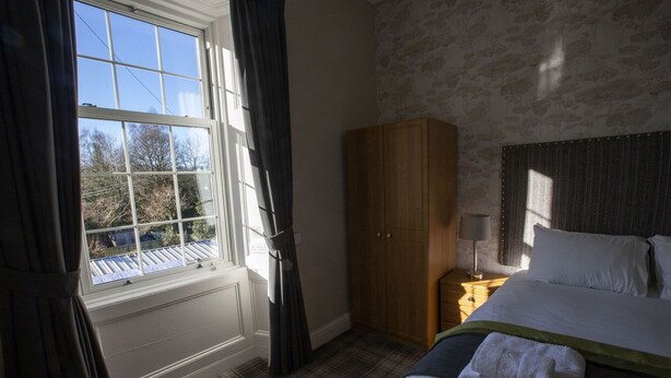 Une chambre à coucher avec un lit, une armoire, une table de chevet, une lampe et une fenêtre avec des rideaux.