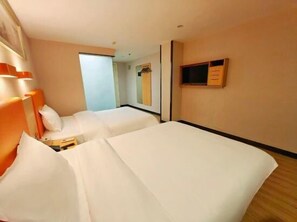 Ein Hotelzimmer mit zwei Betten, einem kleinen Nachttisch, einem Fernseher und einem Spiegel an der Wand.