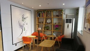 A room with a wooden bookshelf, orange chairs, a wooden table, and a black sofa. - 7 Days Inn Premium Beijing Dongzhimen Airport Express Station (Beijing)