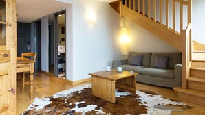 Una sala de estar acogedora con una escalera de madera, un sofá, una mesa de centro y una alfombra de cuero de vaca.