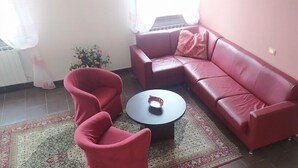Una sala de estar con un sofá rojo, dos sillones rojos, una mesita redonda y un tapete estampado.