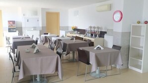 Un comedor con mesas y sillas, un refrigerador, un microondas y un reloj en la pared.