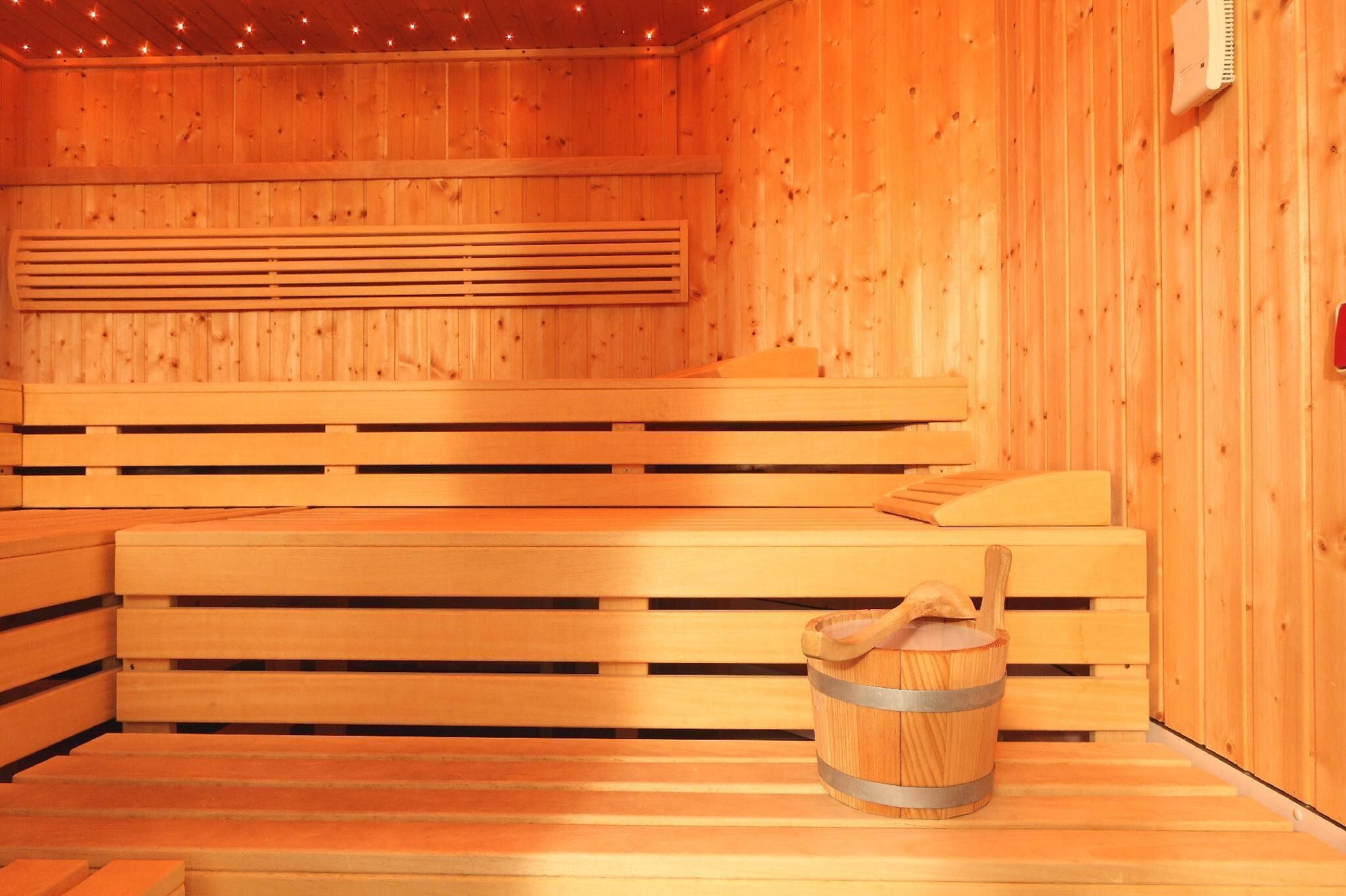 Een houten sauna met banken, een zitbank en een emmer.