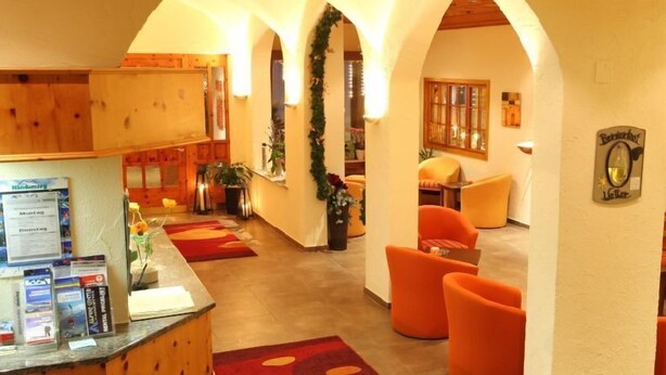 A hotel lobby with a reception desk, orange seating, and a wooden interior. - Bernerhof Swiss Quality Kandersteg Hotel (Kandersteg)