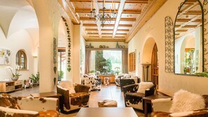 A spacious living room with a wooden ceiling, cowhide upholstered furniture, and a large window providing a view of the outdoors. - Bernerhof Swiss Quality Kandersteg Hotel (Kandersteg)