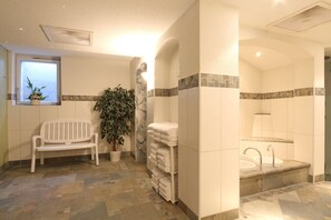 A bathroom with a bench, a potted plant, a towel rack, and a sink with a tiled backsplash. - Bernerhof Swiss Quality Kandersteg Hotel (Kandersteg)