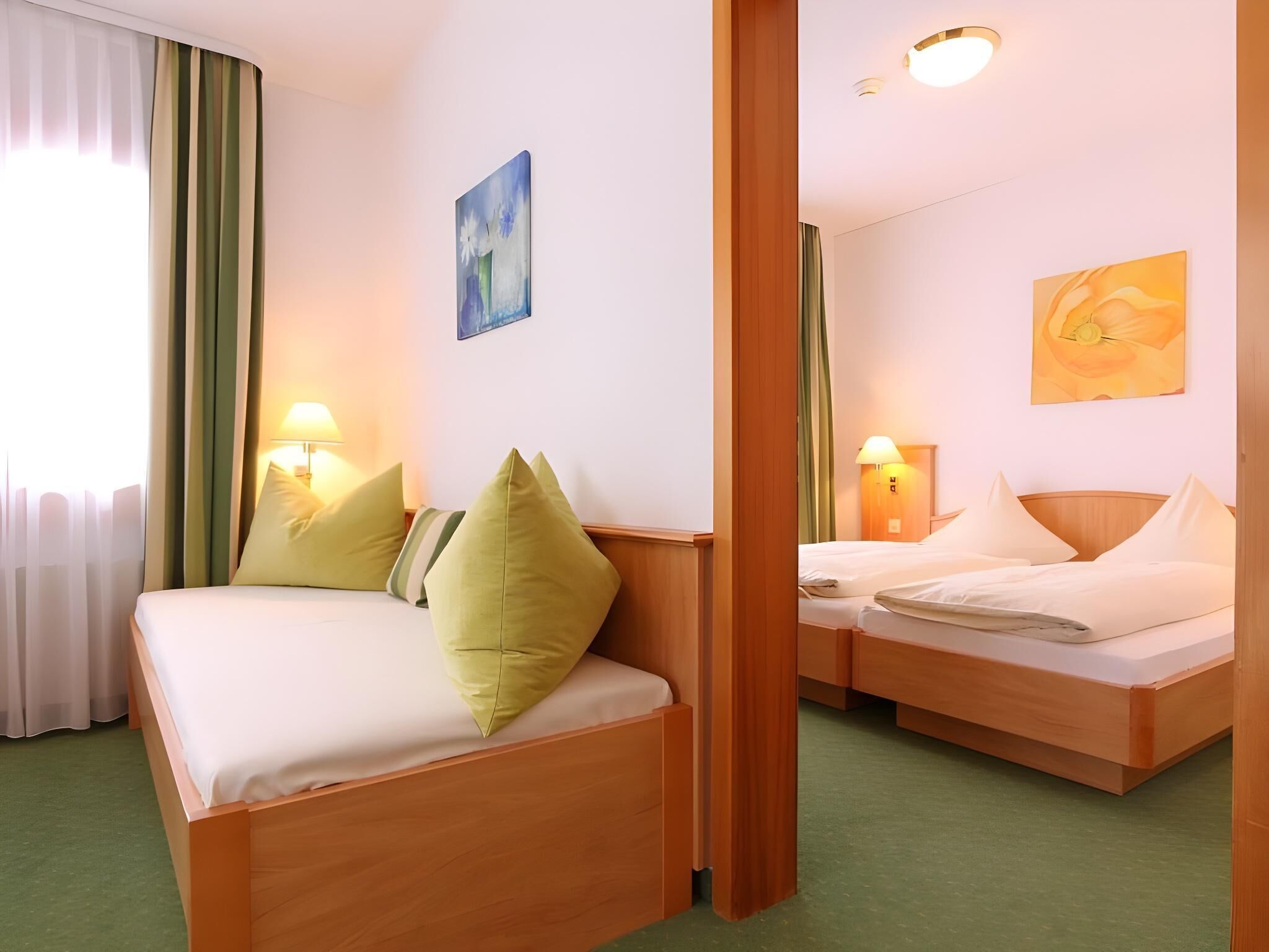 Ein Hotelzimmer mit zwei Betten, grünen Vorhängen und einem Bild an der Wand.