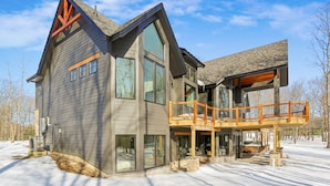 Een modern huis met twee verdiepingen, grote ramen, een houten terras en een stenen fundering.