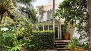 A modern house with a covered outdoor area, surrounded by lush greenery and a palm tree. - Parkview on Sunshine 2 Sunshine Beach (Sunshine Beach)