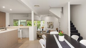 A modern kitchen with a central island, a dining area with a long table, and a staircase leading to an upper level.
