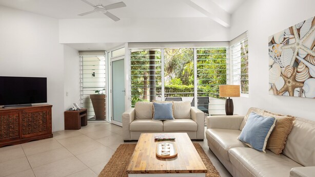 A spacious living room with a television, two sofas, a coffee table, and a large window with a view of greenery. - Parkview on Sunshine 2 Sunshine Beach (Sunshine Beach)