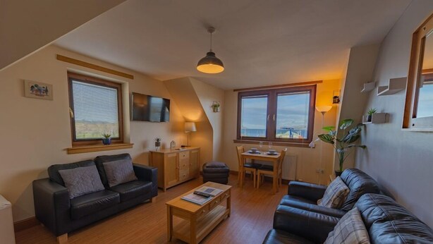 A cozy living room with a sofa, coffee table, and a dining area with a table and chairs. - Quay Head View (Stranraer)