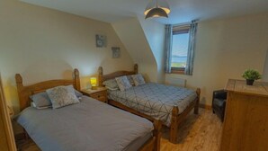 A bedroom with two wooden beds, a nightstand with a lamp, a radiator, and a window with blinds. - Quay Head View (Stranraer)