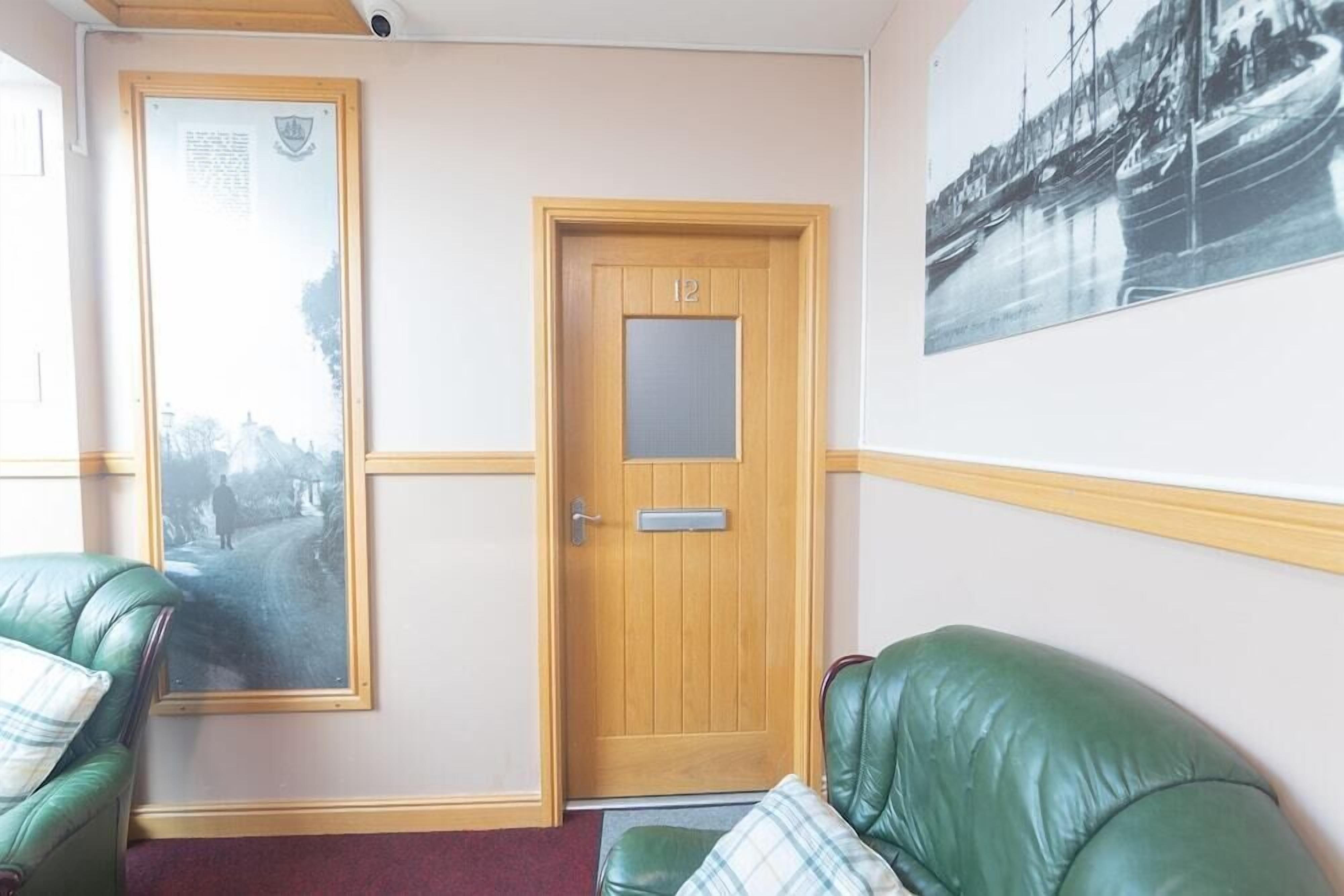 A room with a wooden door marked '12', a framed picture on the wall, and green leather seating.
