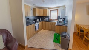 A compact kitchen with wooden cabinets, a black countertop, and a window. - Quay Head View (Stranraer)
