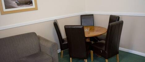 A corner room with a green carpet, a brown sofa, a wooden table, and four black chairs.