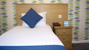 Ein Hotelzimmer mit einem Bett, einem Nachttisch aus Holz, einem Telefon und einer Wand mit geometrischem Muster.