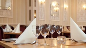 Ein Esstisch mit Weingläsern, einer Kerze und Besteck in einem Restaurant, das mit Holzvertäfelung und Wandleuchten gestaltet ist.
