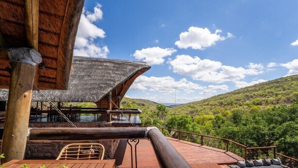 Um deck de madeira com vista para um vale verdejante e um céu azul límpido.