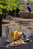 Un desayuno con croissants, jugo y condimentos sobre una mesa al aire libre.