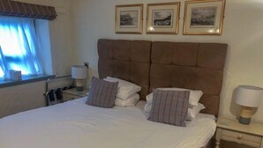A neatly made bed with white linens and striped pillows, a brown upholstered headboard, and a bedside table with a lamp. - Hoops Country Inn & Hotel (Bideford)