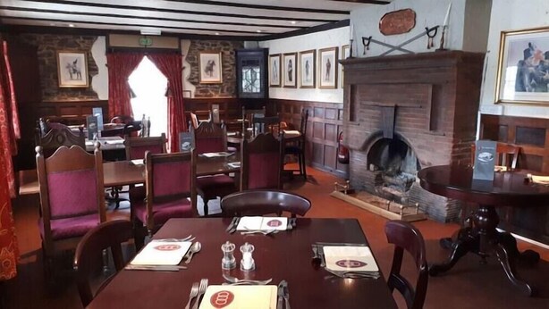 A restaurant with wooden tables and chairs, a stone fireplace, and framed pictures on the walls. - Hoops Country Inn & Hotel (Bideford)