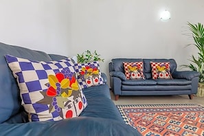 A living room with a dark blue sofa, two patterned cushions, a small plant, and a patterned rug. - Ghibli Hotel (San Vito Lo Capo)