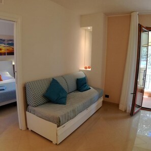 Ein modernes, kompaktes Wohnzimmer mit einer Couch, einem kleinen Tisch und Blick ins Freie.