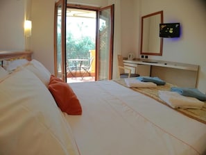 A hotel room with a bed, a desk, a chair, and a balcony with a table and chairs.