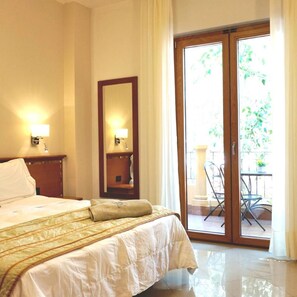 Habitación de hotel con cama, mesita de noche, espejo y puerta corrediza de vidrio que da a un espacio exterior con una silla y una mesa.