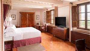 Een hotelkamer met een bed, een bureau met een televisie, een stoel, een klein tafeltje met een vaas en een raam met gordijnen.