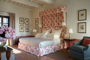 Une chambre à coucher avec un grand lit, des rideaux à motifs floraux, des reproductions botaniques encadrées accrochées au mur et un vase rempli de fleurs.