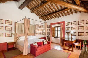 Un lit à baldaquin, un canapé rouge, un bureau avec une chaise et un miroir.