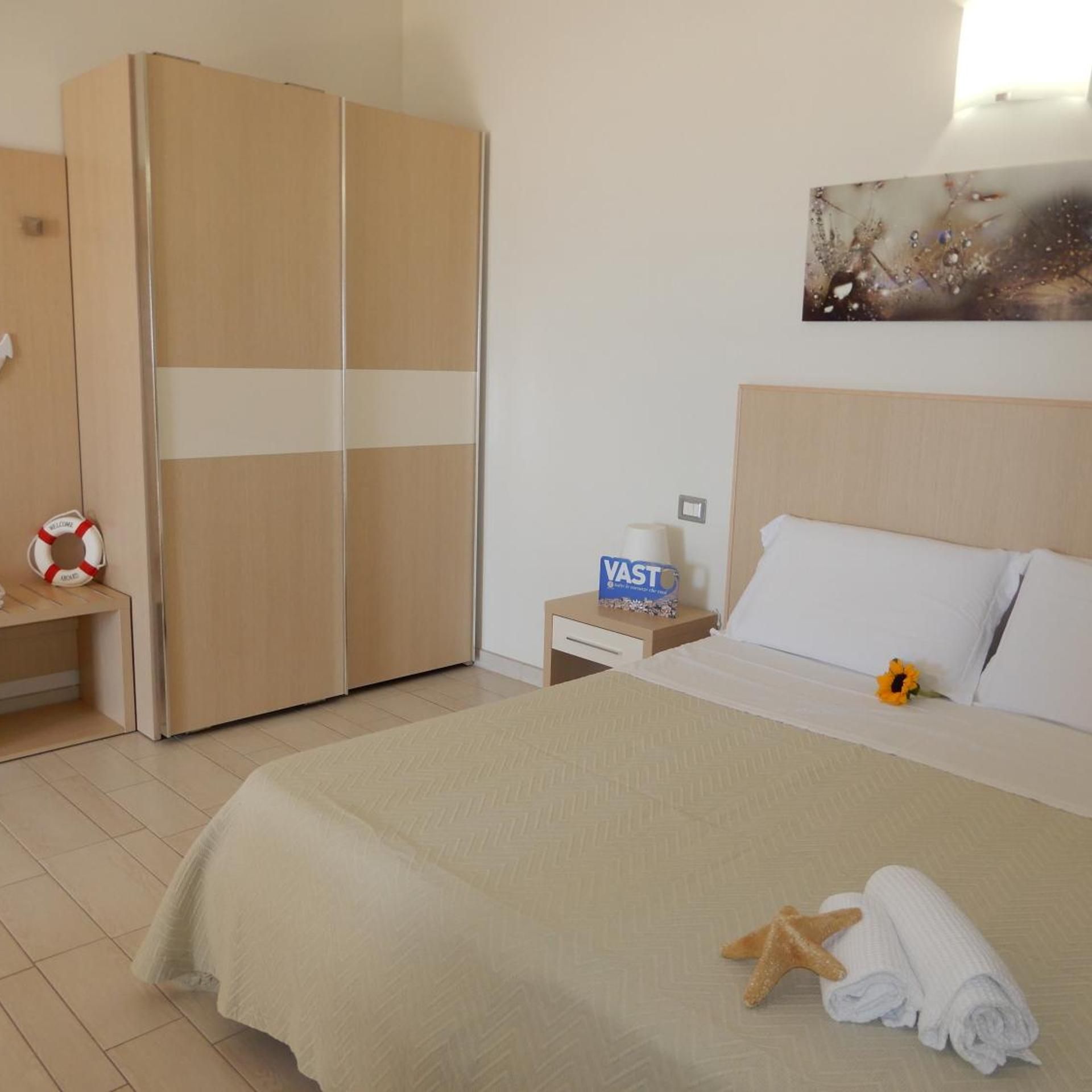 Une chambre d’hôtel avec un lit, une armoire, une table de chevet, une grande enseigne et un tableau accroché au mur.
