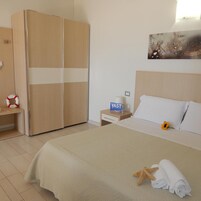 Una camera d'albergo con un letto, un armadio, un comodino, un cartello VAST e un quadro appeso al muro.