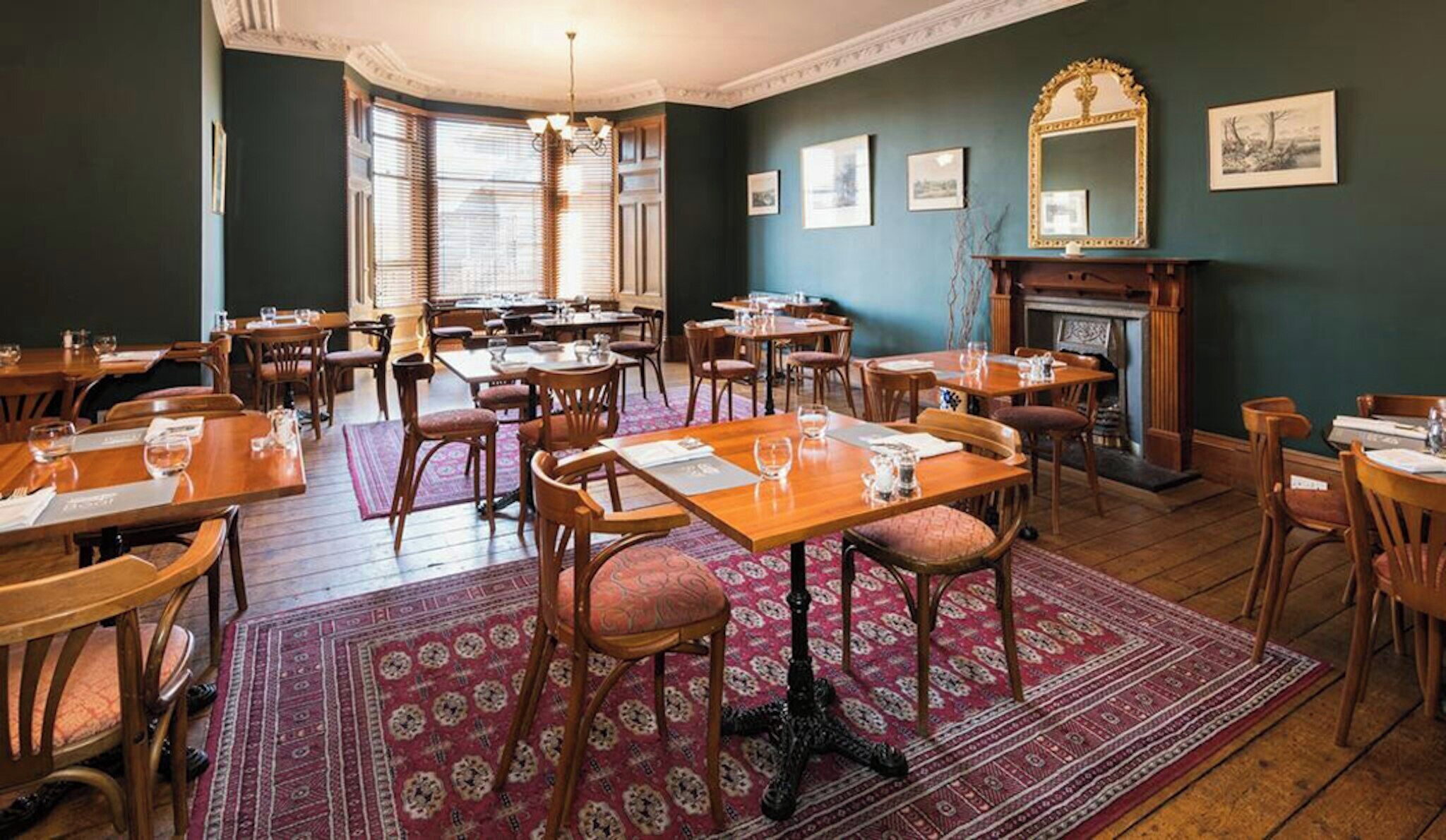 A dining area with multiple tables and chairs, a patterned rug, a fireplace, and framed pictures on the walls.