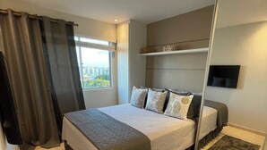 Une chambre moderne avec un grand lit, un téléviseur à écran plat fixé au mur et une vue sur la ville par la fenêtre.