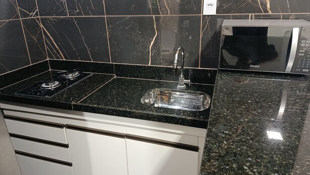 A kitchen with a black marble backsplash, a stainless steel sink, and a microwave. - Studio apartment with bedroom, kitchen, and bathroom, comfortable and cozy, independent. (Contagem)