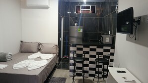 A compact room with a bed, a small kitchenette, a TV, and a checkered bar stool. - Studio apartment with bedroom, kitchen, and bathroom, comfortable and cozy, independent. (Contagem)