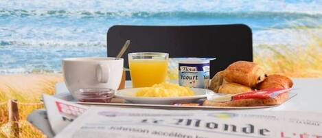 Ontbijtproducten op een tafel met een krant, een stoel en uitzicht op de oceaan.