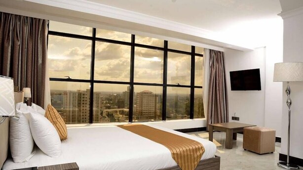 Habitación de hotel con un ventanal grande, una cama, un escritorio, una silla y un televisor.