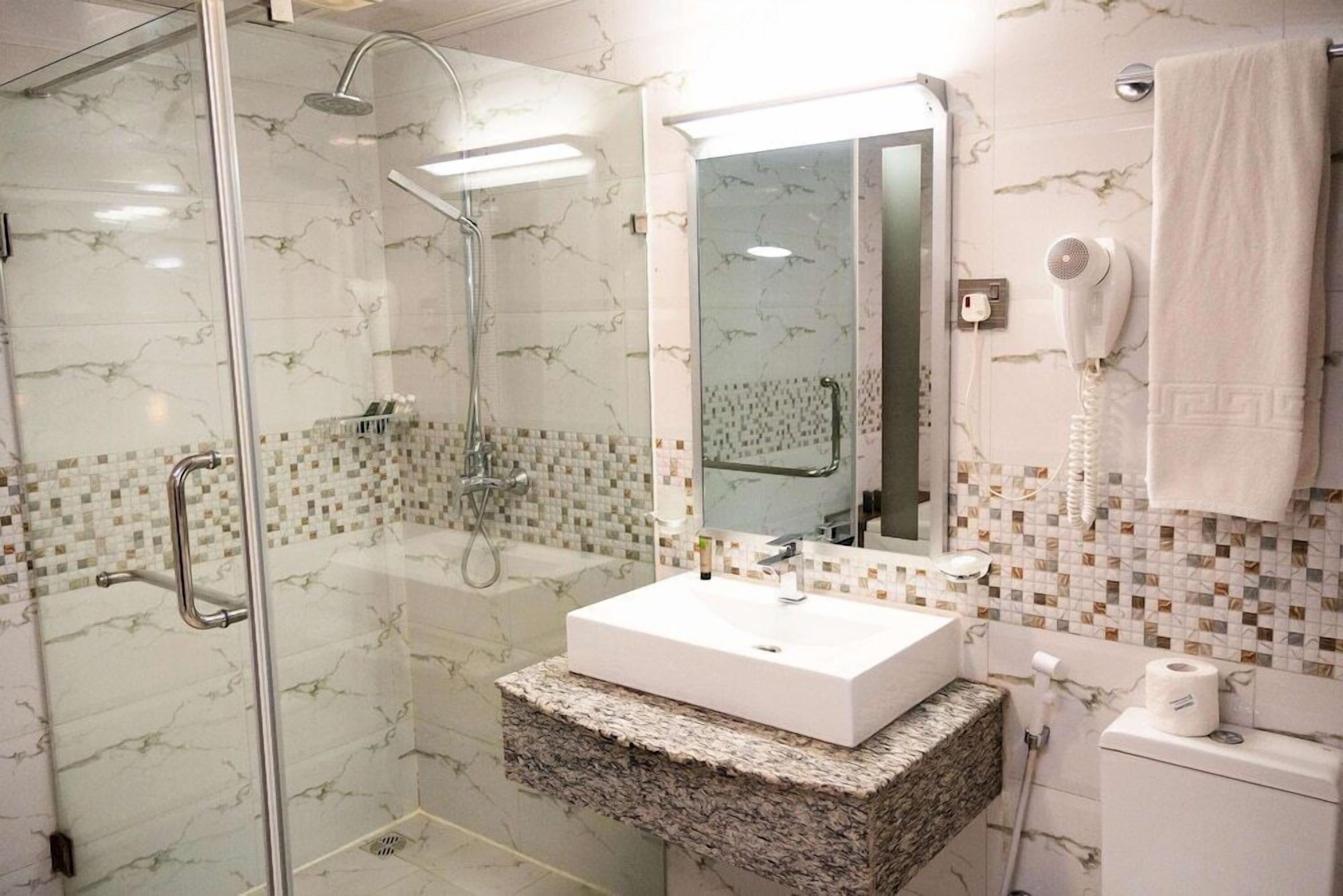 Un baño moderno con ducha de vidrio, un lavabo blanco y pared con azulejos de mármol.