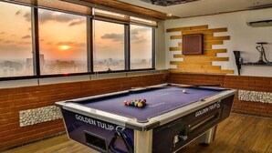 Una mesa de billar con el rótulo 'GOLDEN TULIP' y vista a un paisaje urbano a través de amplios ventanales.