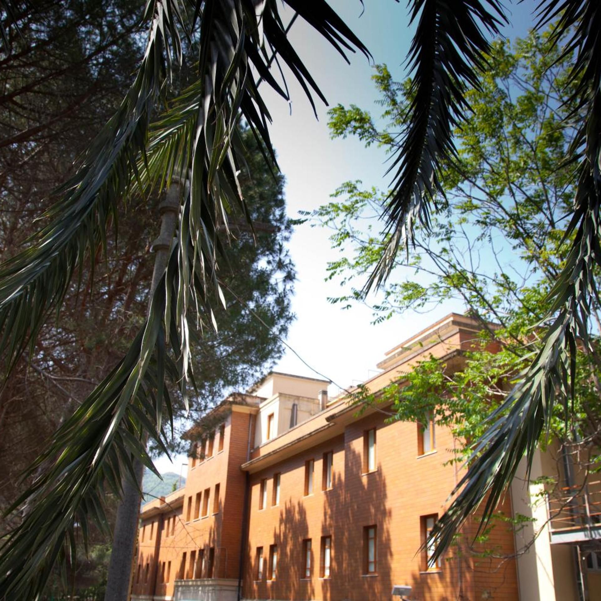Un edificio a più piani con facciata in mattoni, circondato da alberi e vegetazione.