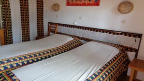 A bedroom with two beds, a wooden headboard, a small table, and a wall with decorative plates. - Maya (Cap Skirring)